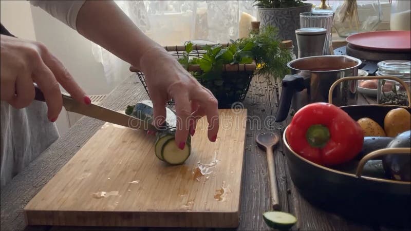 Women hands cutting zucchini on wooden cutting board on kitchen table at window