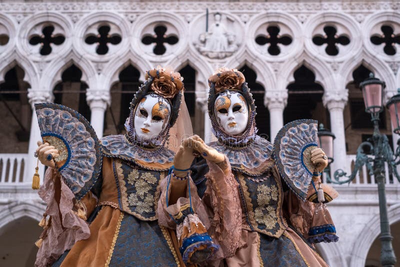 Women holding fan and wearing mask and ornate gold and black costume standing in front of the Doges Palace during Venice Carnival, Carnivale di Venezia, Italy. Women holding fan and wearing mask and ornate gold and black costume standing in front of the Doges Palace during Venice Carnival, Carnivale di Venezia, Italy