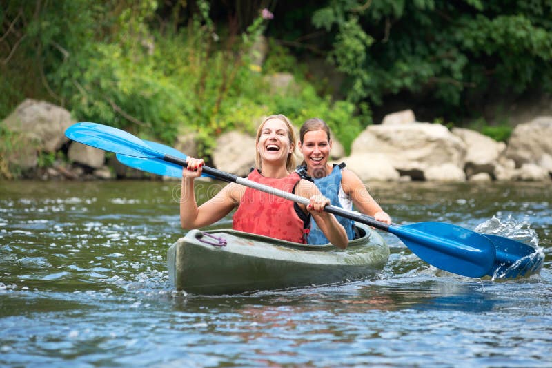 Women kayaking. Two smiling young women kayaking down a river stock image