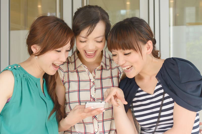 Group of smiling Asian women looking at something on a cellphone.