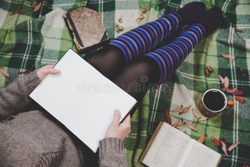 Women& x27; mani e piedi di s in maglione ed in calzini accoglienti che tengono tazza di caffè caldo, sedentesi sul plaid con il immagine stock libera da diritti Women& x27; mani e piedi di s in maglione ed in calzini accoglienti che tengono tazza di caffè caldo, sedentesi sul plaid con il immagine stock libera da diritti
