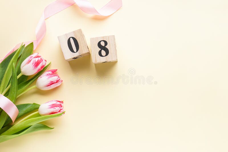 Women`s day, a bouquet of fresh tulips in a pink ribbon with a wooden calendar on a yellow background. 8 March, International stock image Women`s day, a bouquet of fresh tulips in a pink ribbon with a wooden calendar on a yellow background. 8 March, International stock image