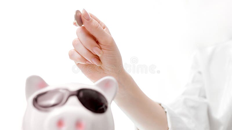 Women`s hand from top to bottom puts a coin in the piggy bank pig with glasses