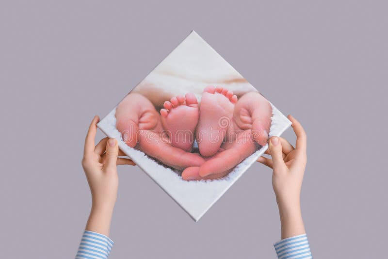 Women`s hands hang a family photo of a newborn`s legs printed on canvas on a gray wall