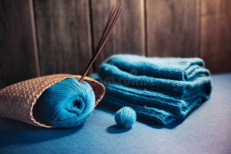 Women`s hobby. Crochet and knitting. Working space. Blue yarn in basket, knitting needles, scissors, crochet hooks on the wooden background  in the cozy home in rustik style.