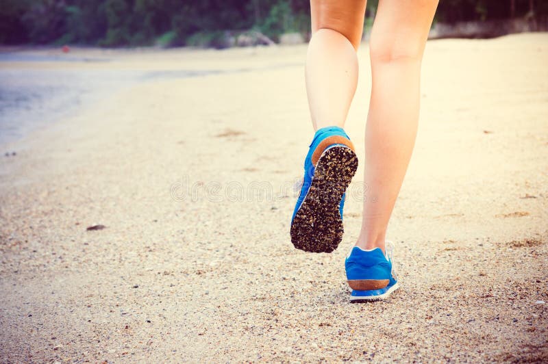 Women's legs running or walking along the beach trail with blue sport shoes. Women's legs running or walking along the beach trail with blue sport shoes.