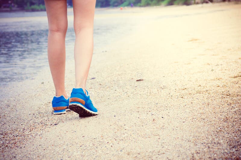 Women's legs running or walking along the beach trail with blue sport shoes. Women's legs running or walking along the beach trail with blue sport shoes.