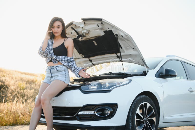 Women talking on the phone about problem with her car she can& x27;t. Young sexy girl consults on the phone during car repair. open the hood of the gray car.