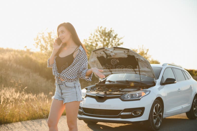 Women talking on the phone about problem with her car she can& x27;t. Young sexy girl consults on the phone during car repair. open the hood of the gray car.