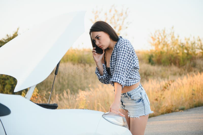 Women talking on the phone about problem with her car she can& x27;t. Young sexy girl consults on the phone during car repair. open the hood of the gray car.