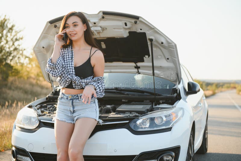 Women talking on the phone about problem with her car she can& x27;t. Young sexy girl consults on the phone during car repair. open the hood of the gray car.