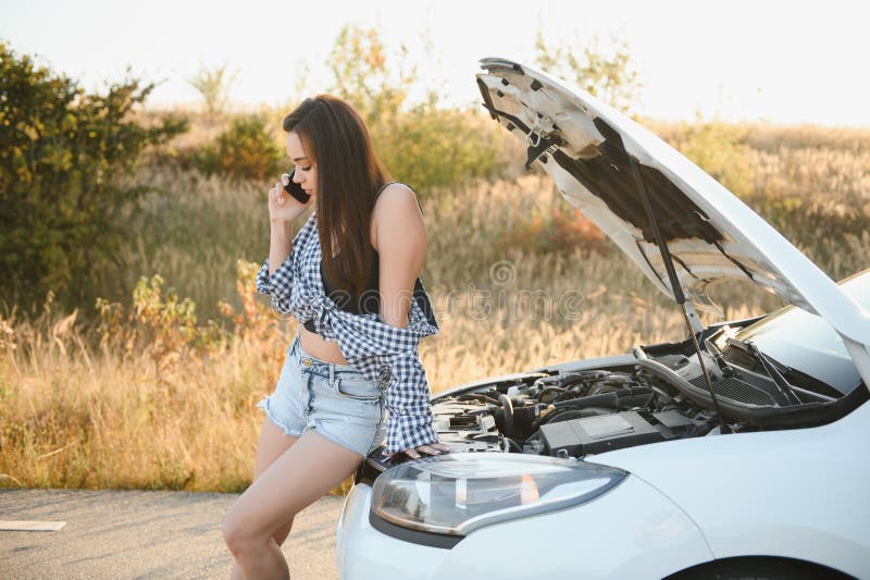 Women talking on the phone about problem with her car she can& x27;t. Young sexy girl consults on the phone during car repair. open the hood of the gray car.