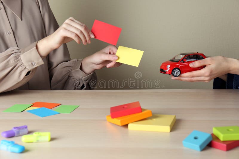 Women with toy car and color papers at wooden table indoors, closeup. ABA therapy concept royalty free stock images