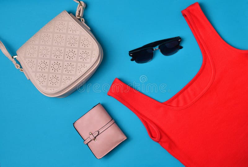 Women& x27;s clothing and accessories laid out on a blue background. Red T-shirt, purse, bag, sunglassesï»¿ Top View. Flat lay