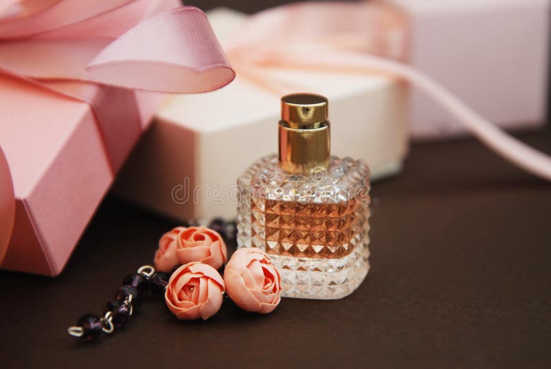 Women& x27;s Pink Perfume in Beautiful Bottle and Artificialt Flowers Bracelet on Brown Background with gift boxes on Background.