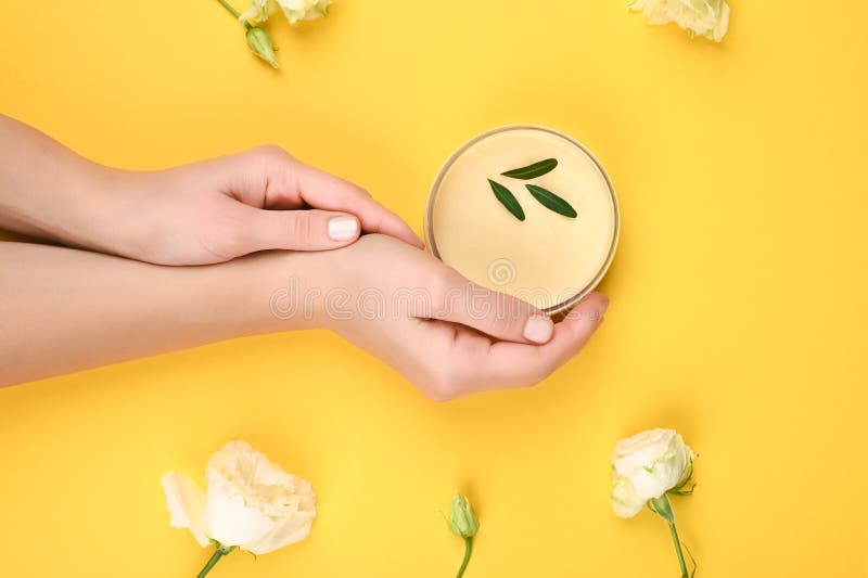 Womens hands hold a jar of natural cosmetics. cream. eco cosmetics. hands near flowers on a yellow background. cream in the hands.