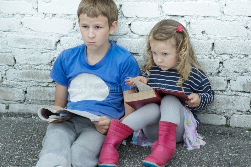 Wondering sibling children sitting on asphalt ground with books in hands royalty free stock images Wondering sibling children sitting on asphalt ground with books in hands royalty free stock images
