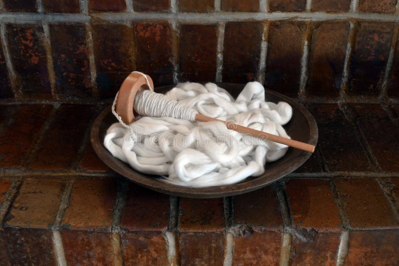 This is a wood bowl filled with natural white cotton pencil roving with a wood spindle filled with hand spun cotton yarn on a red brick background. This is a wood bowl filled with natural white cotton pencil roving with a wood spindle filled with hand spun cotton yarn on a red brick background.