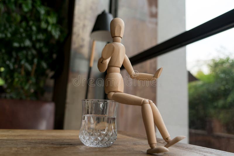 Wood man is sitting on a glass of water royalty free stock photos