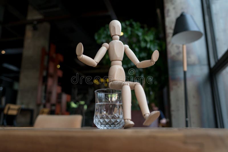 Wood man is sitting on a glass of water royalty free stock image