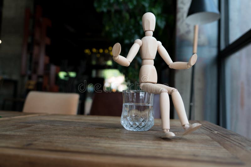 Wood man is sitting on a glass of water stock image