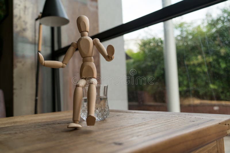 Wood man is sitting on a glass of water royalty free stock photography