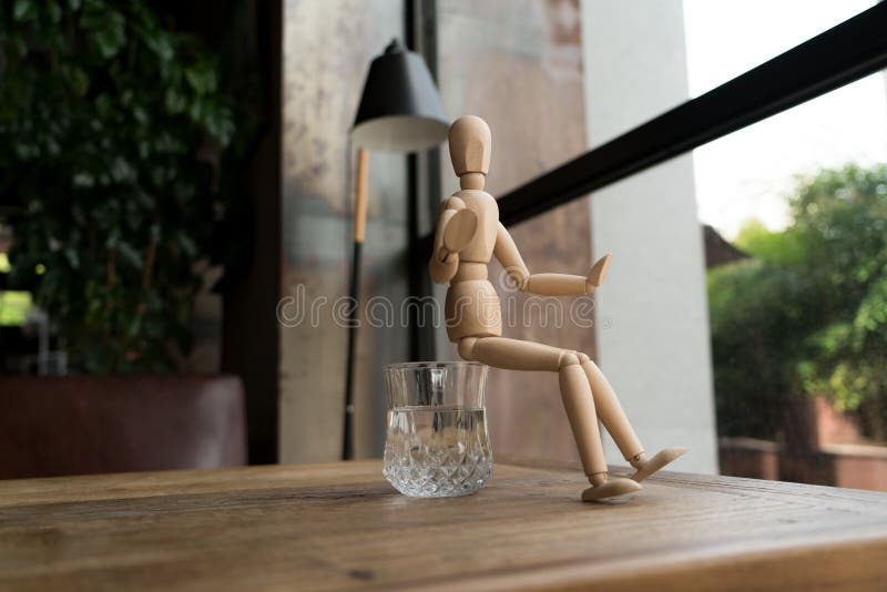 Wood man is sitting on a glass of water royalty free stock photo