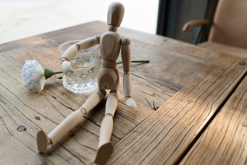 A wood man is sitting and put the arm on the glass of water stock photos