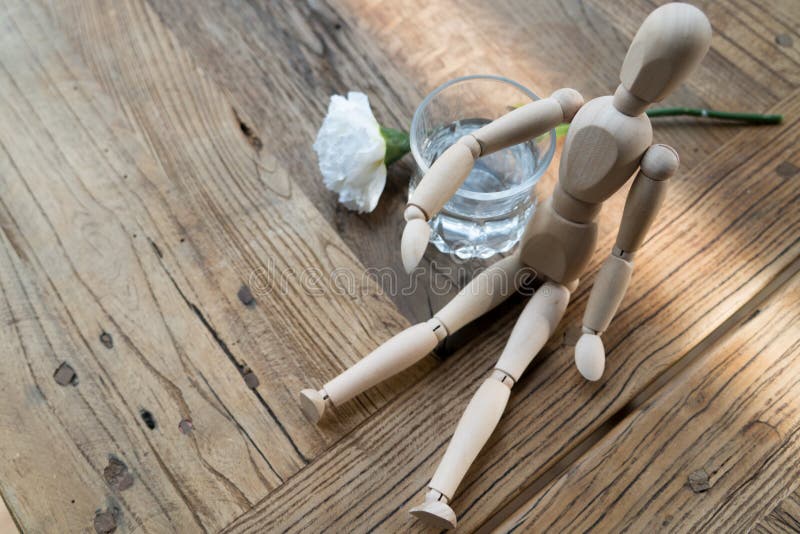 A wood man is sitting and put the arm on the glass of water stock photo
