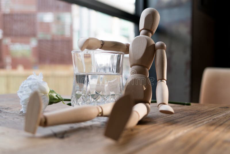 A wood man is sitting and put the arm on the glass of water stock image
