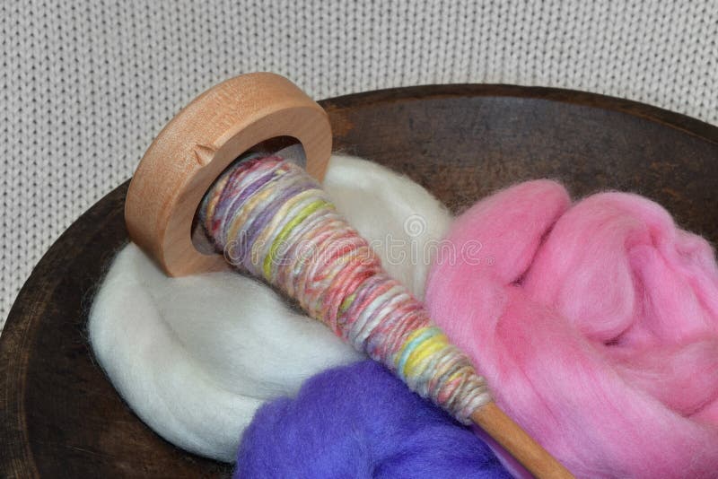 This is a photo of a wooden spindle with colorful hand spun yarn in a wooden bowl full of wool roving bundles. This is a photo of a wooden spindle with colorful hand spun yarn in a wooden bowl full of wool roving bundles