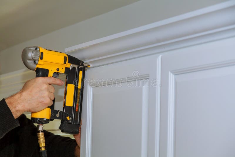 Wood working using brad nail gun to Crown Moulding on white kitchen cabinets framing trim