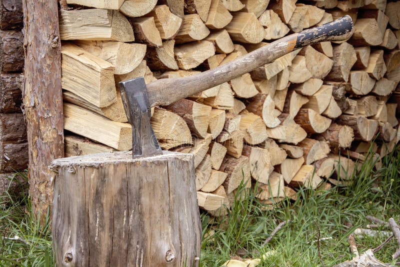 A woodcutter`s metal axe with a wooden handle is stuck in a log for chopping wood against the background of a split tree stacked