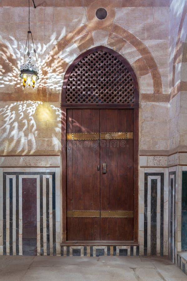 Wooden arched door on stone wall decorated with marble panels and lantern shadows on the wall, Old Cairo, Egypt stock photos