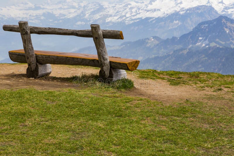 Wooden bench on green grass with view of snow on peak of high mo