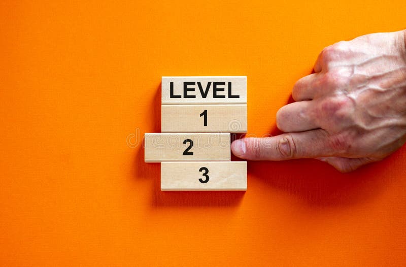 Wooden blocks form the words `level, 1, 2, 3,` on orange background. Male hand. Beautiful background. Business concept