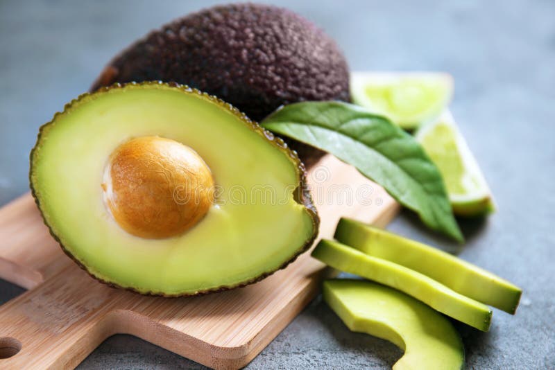 Wooden board with ripe avocados on grey textured background