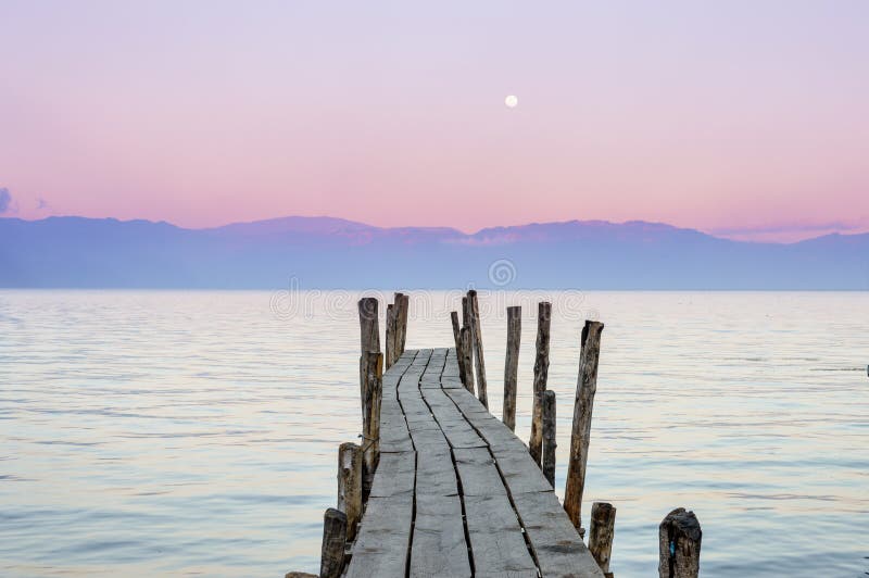 Little wooden boat dock with the pink sunset sky on the background in Lake Atitlan, Guatemala. Little wooden boat dock with the pink sunset sky on the background in Lake Atitlan, Guatemala