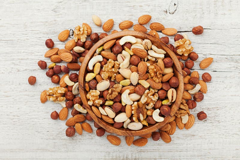 Wooden bowl with mixed nuts on white table top view. Healthy food and snack. Walnut, pistachios, almonds, hazelnuts and cashews. stock images Wooden bowl with mixed nuts on white table top view. Healthy food and snack. Walnut, pistachios, almonds, hazelnuts and cashews. stock images
