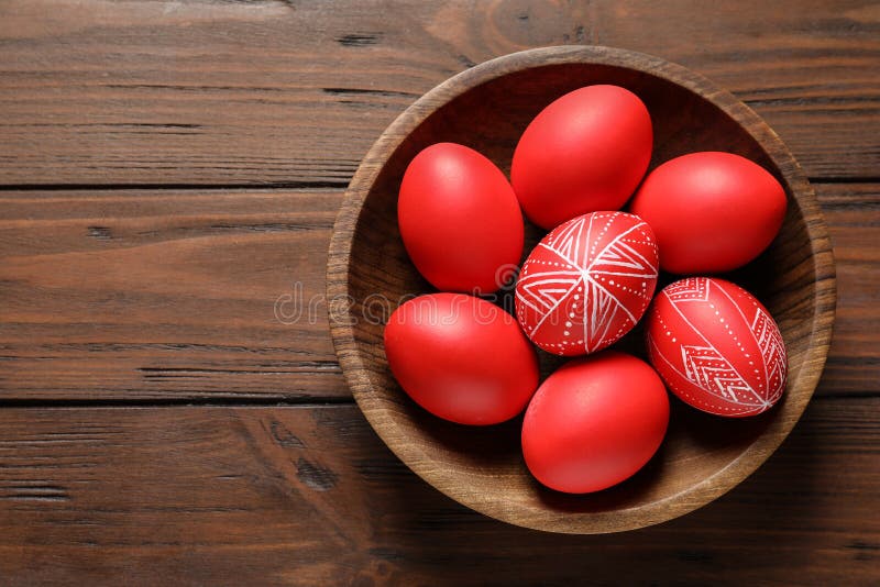 Wooden bowl with painted red Easter eggs on table, top view.