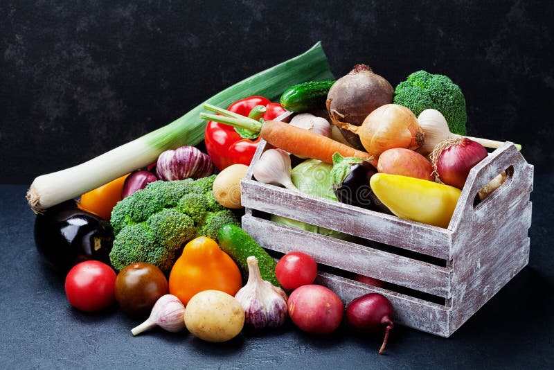 Wooden box with autumn harvest farm vegetables and root crops on black kitchen table. Healthy and organic food.