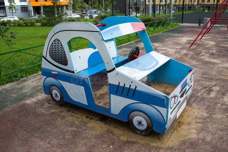 A wooden car of blue, blue and white color against the background of a green lawn and a multi-storey building. Playgrounds