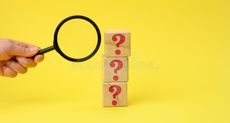 Wooden cubes with question marks and a female hand holds a magnifying glass on a yellow background. The concept of finding answers royalty free stock image
