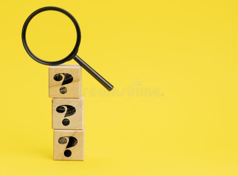 Wooden cubes with question marks and a magnifying glass on a yellow background. The concept of finding answers to unknown stock photos