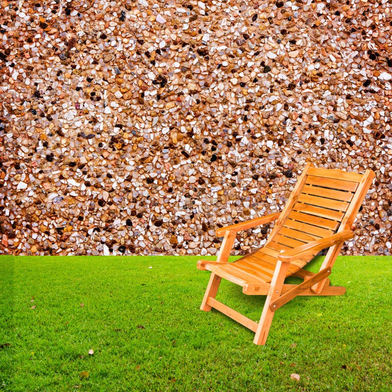 Wooden deck chair on green grass with stone wall royalty free stock photos