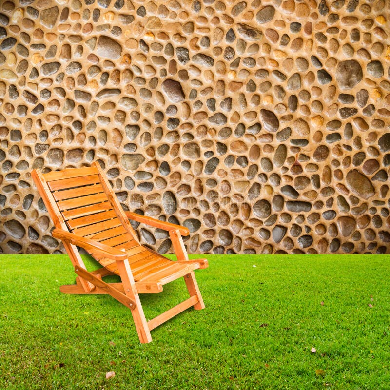 Wooden deck chair on green grass with stone wall stock image