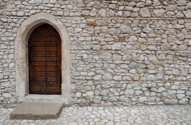 A wooden door with pointed gothic style arch in a stone wall. The brown wooden back door or entrance to an old building is located in a wall with white stock images A wooden door with pointed gothic style arch in a stone wall. The brown wooden back door or entrance to an old building is located in a wall with white stock images
