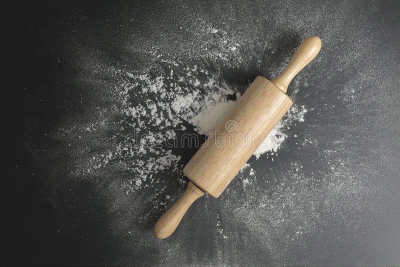 Wooden Dough Roller on the Black Table with Flour Spread Stock Photo