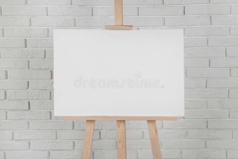 Wooden easel with blank canvas near white brick wall. Wooden easel with blank canvas near white brick