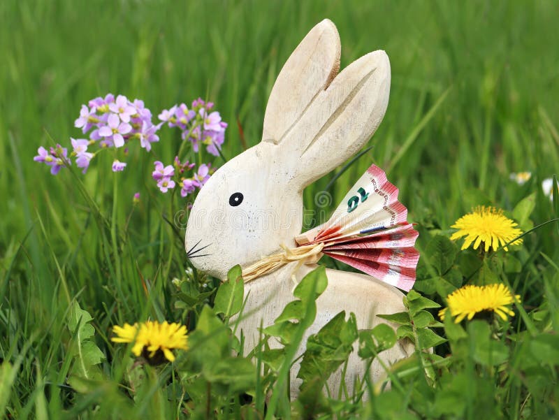wooden easter bunny with euro banknote in green spring meadow between flowers, money gifts at easter concept image